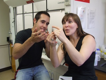 A young white man is enthusiastically describing something to a young white women, who is very interested. Both are wearing casual attire, in a lab.